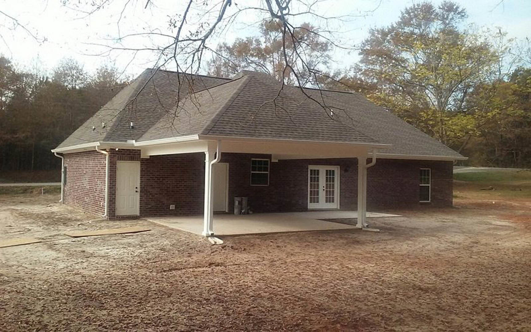 Covered patio with white paneled door and black hardware, multi-pane window, white exterior walls with black trim, dirt patch in foreground, small white cottage visible in