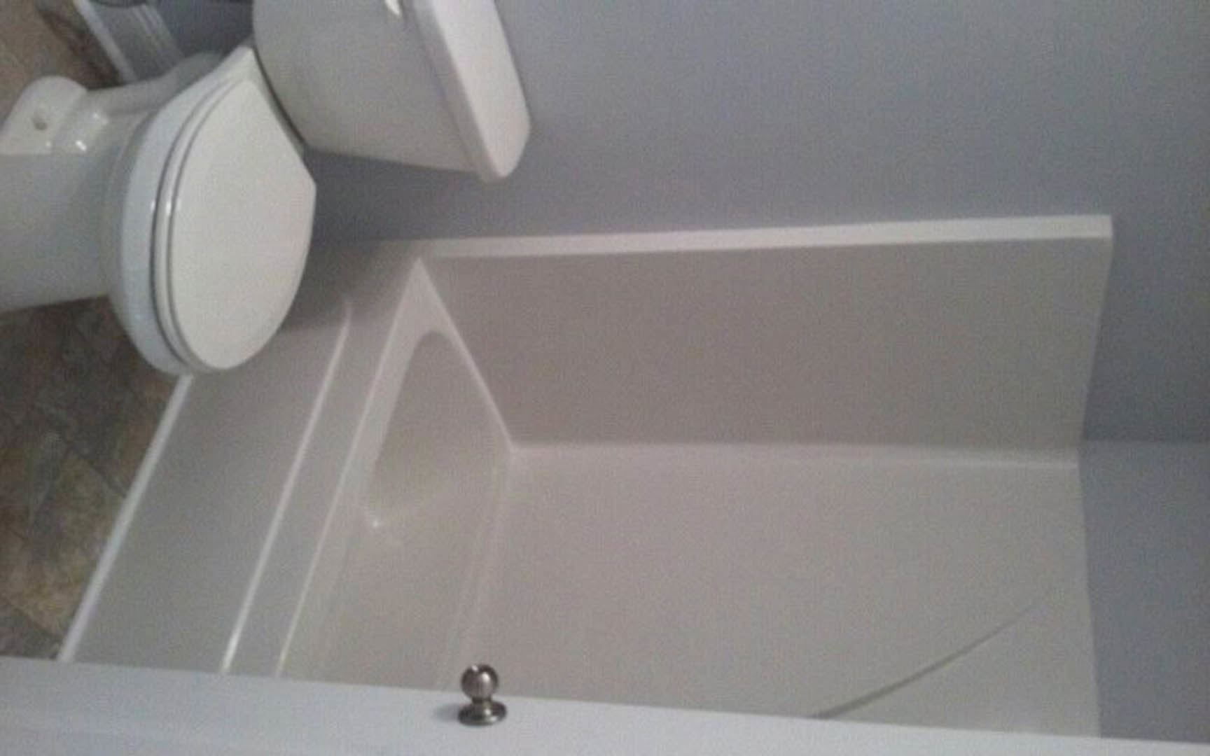 White bathtub with silver faucet next to a white toilet, set against a white tiled wall with matching border.