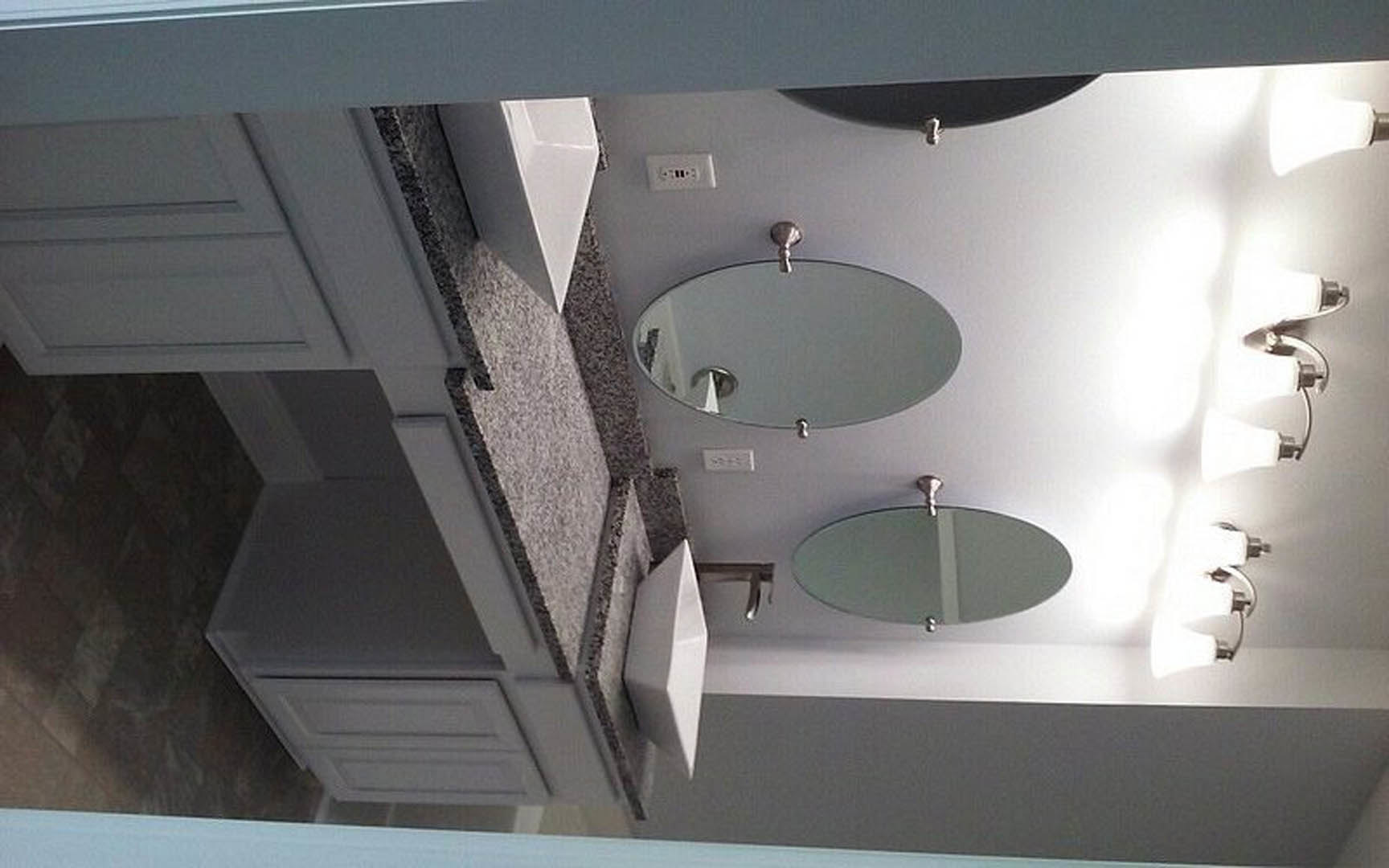 White bathroom vanity with round wall-mounted mirror, chrome faucet, and marble countertop against light-colored tile backsplash