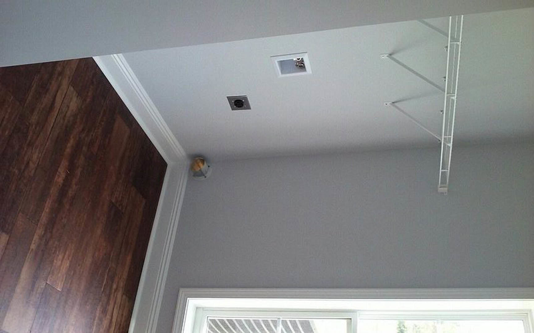 White plaster wall with a modern ceiling fixture, wood flooring, white door, and white ladder in a minimalist room.