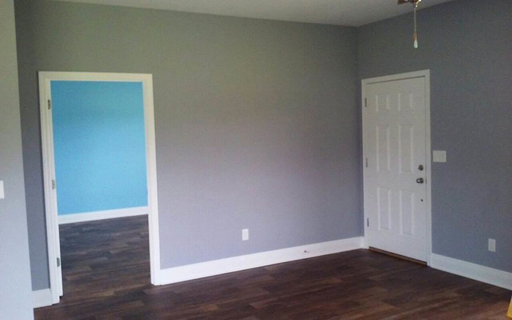 Blue accent wall and white door with silver knobs, dark wood flooring, white baseboard trim