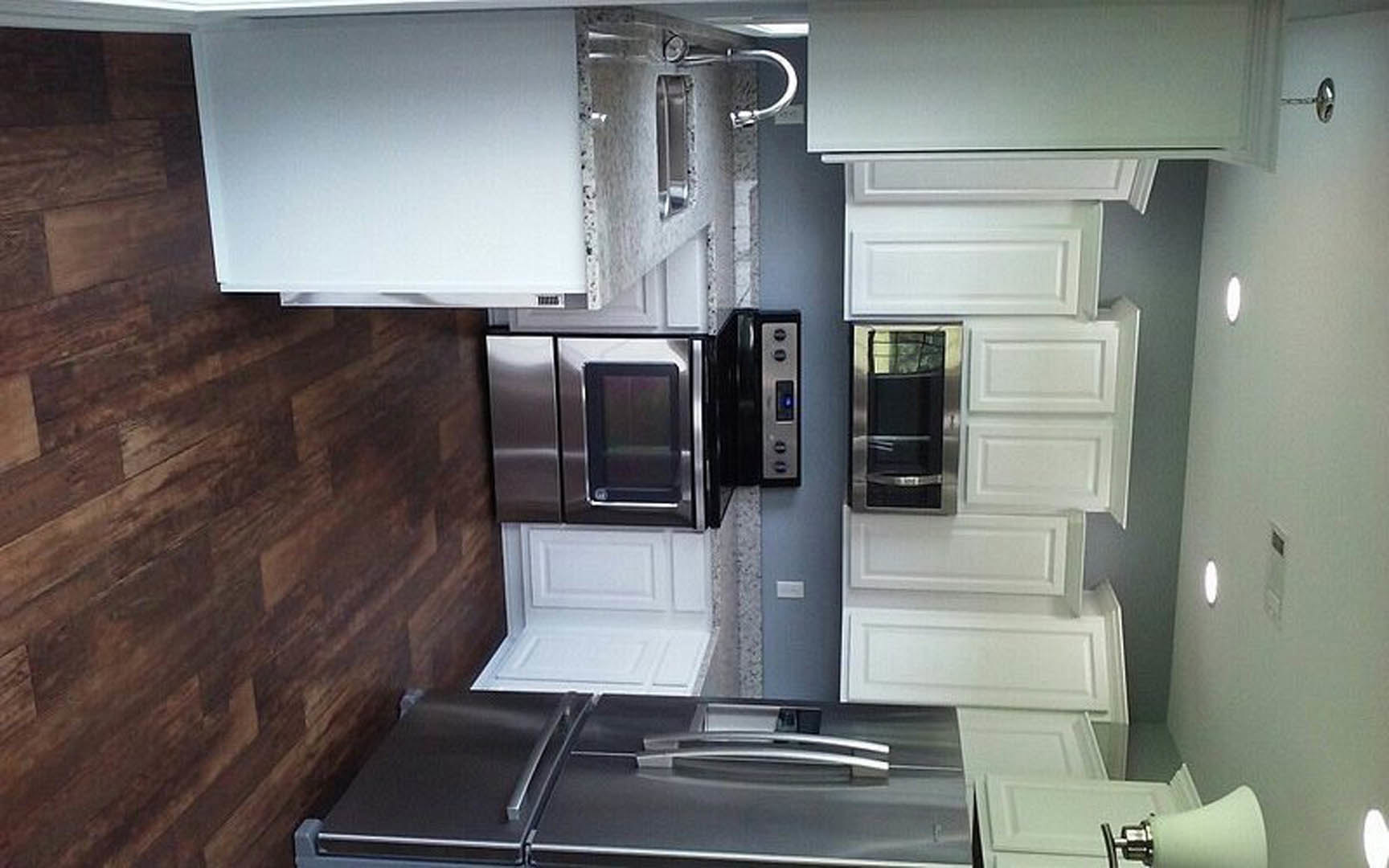 White kitchen cabinets, stainless steel refrigerator with glass door, black stovetop, white lamp, white countertop with black border