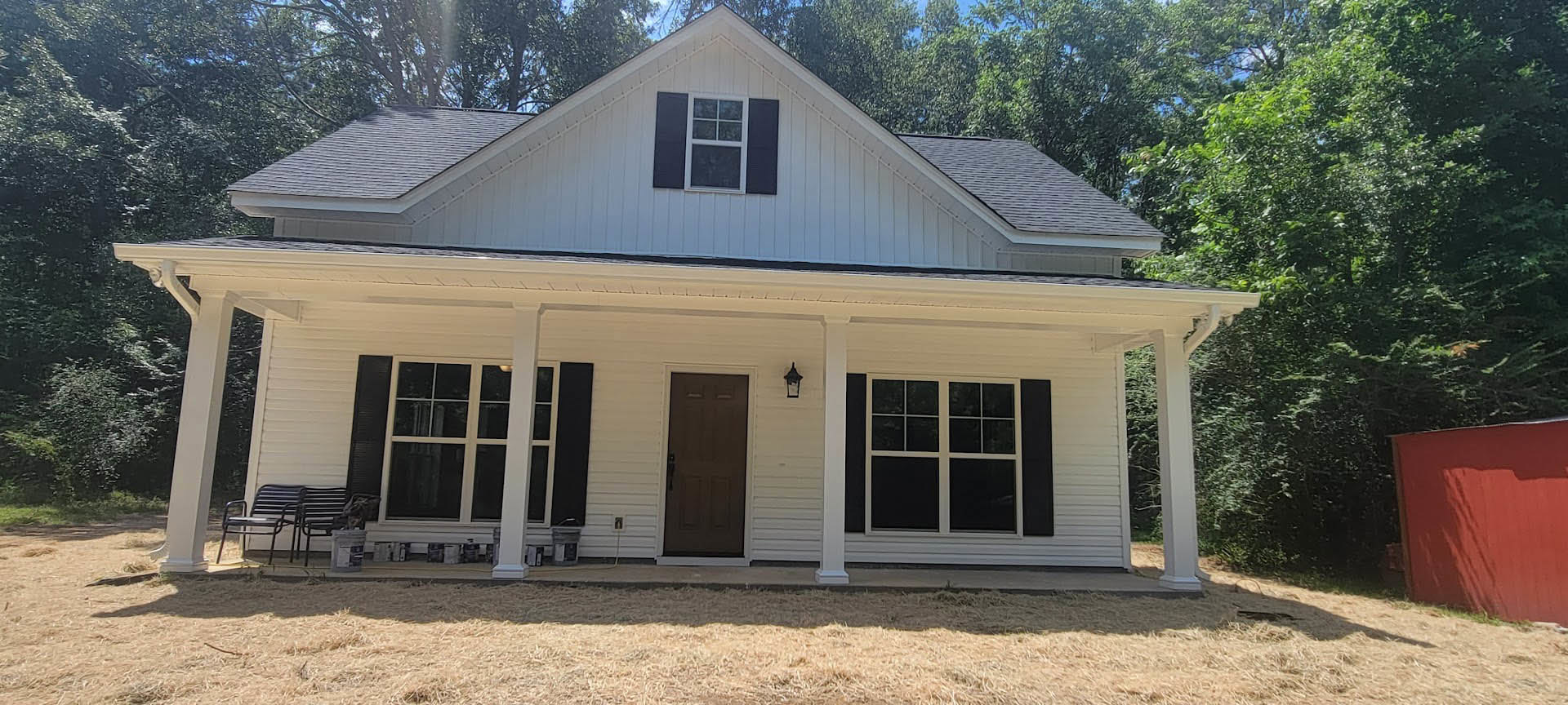 White siding house with covered porch, black front door, white-framed windows, black outdoor chair and table, tree and garden visible in front yard.