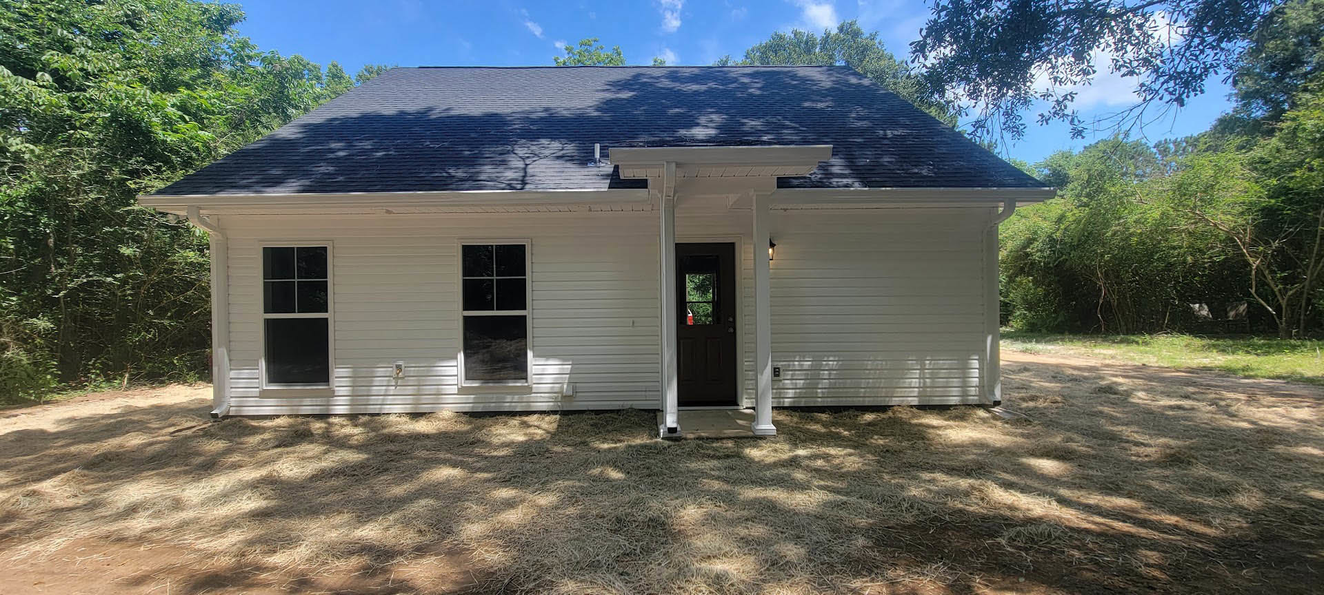 White siding house with black shingle roof, black front door with window, white-framed windows, small grass patch in front, cloudy sky overhead.