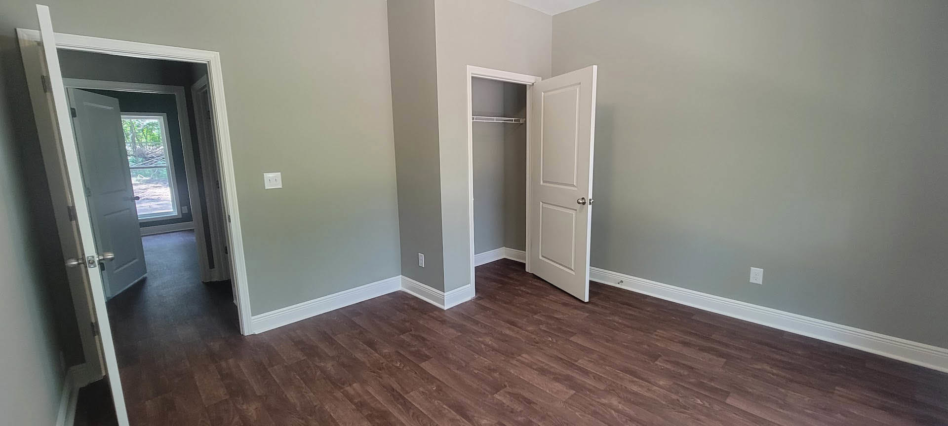 White paneled door with silver handle open onto wood laminate flooring, white plaster walls, and a light switch visible nearby.