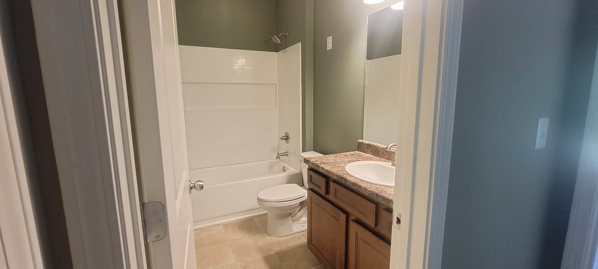 Modern bathroom featuring white porcelain sink and toilet, chrome faucet, wall-mounted mirror, light gray tile walls, and minimalist cabinetry