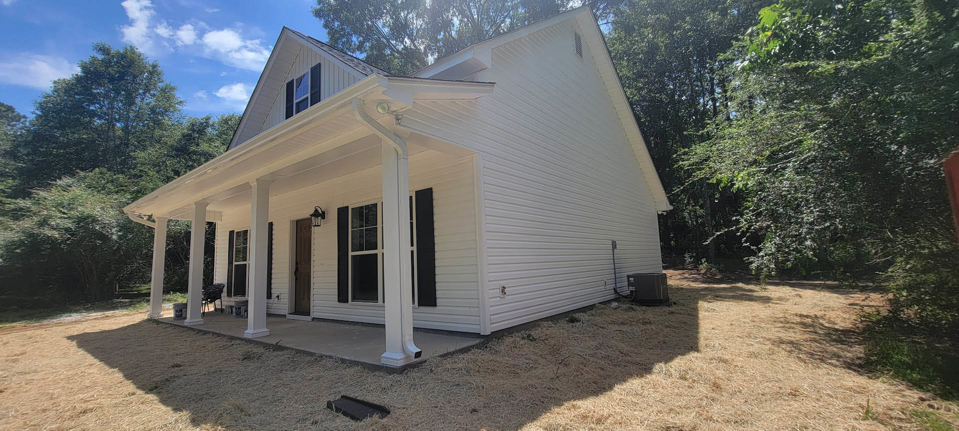 White siding house with two spacious porches, white framed windows, black gutter, surrounded by trees under a partly cloudy sky