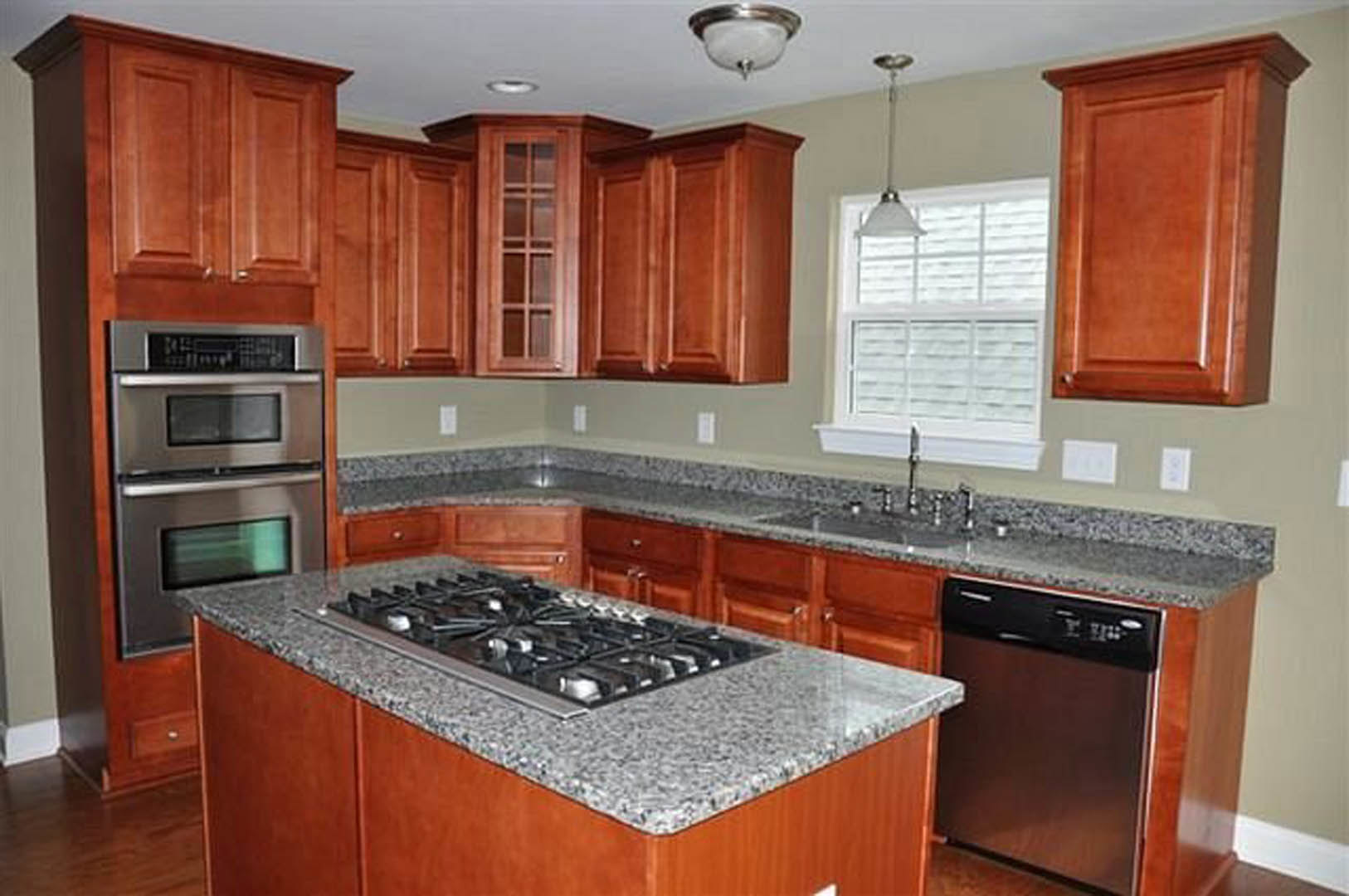 Granite countertops, stainless steel appliances, white cabinetry, double oven, stove top, dishwasher, modern light fixture in a contemporary kitchen