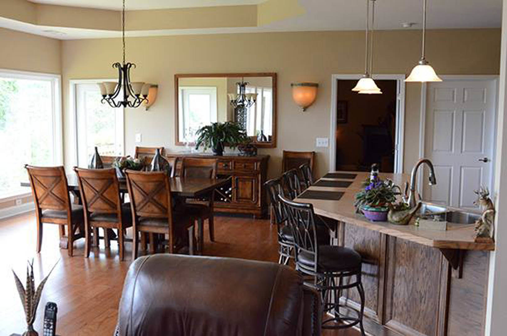 Dining room featuring a spacious kitchen island with white countertops, a large wooden dining table surrounded by upholstered chairs, brown sofa with textured fabric, potted plant