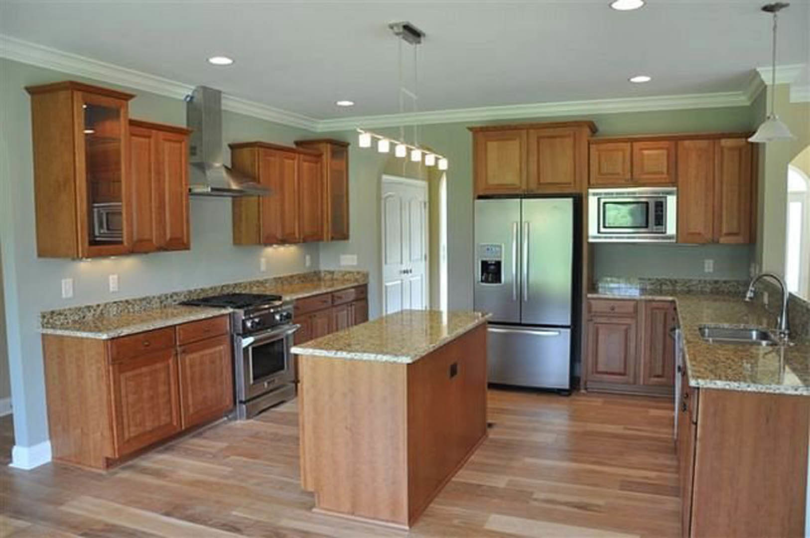 Kitchen with natural wood cabinets, stainless steel refrigerator, marble-topped island, and light-colored flooring