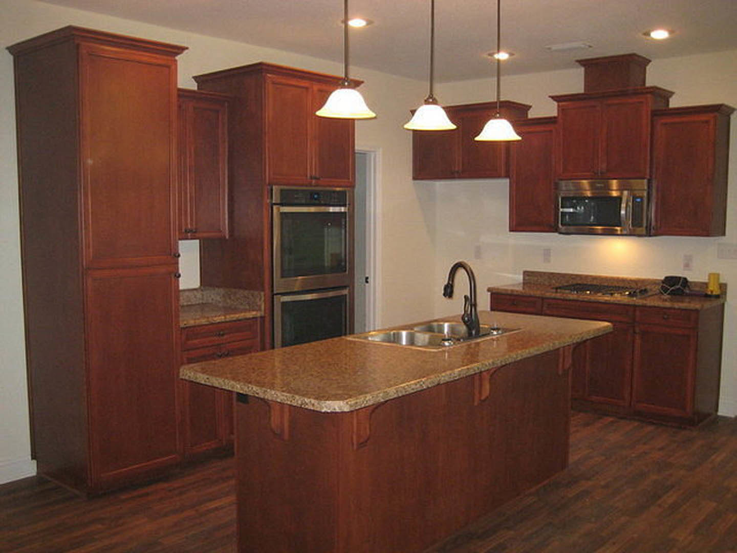 Spacious kitchen featuring a large central island with built-in sink and black faucet, white cabinetry, stone countertops, stainless steel microwave, pendant ceiling lights, and