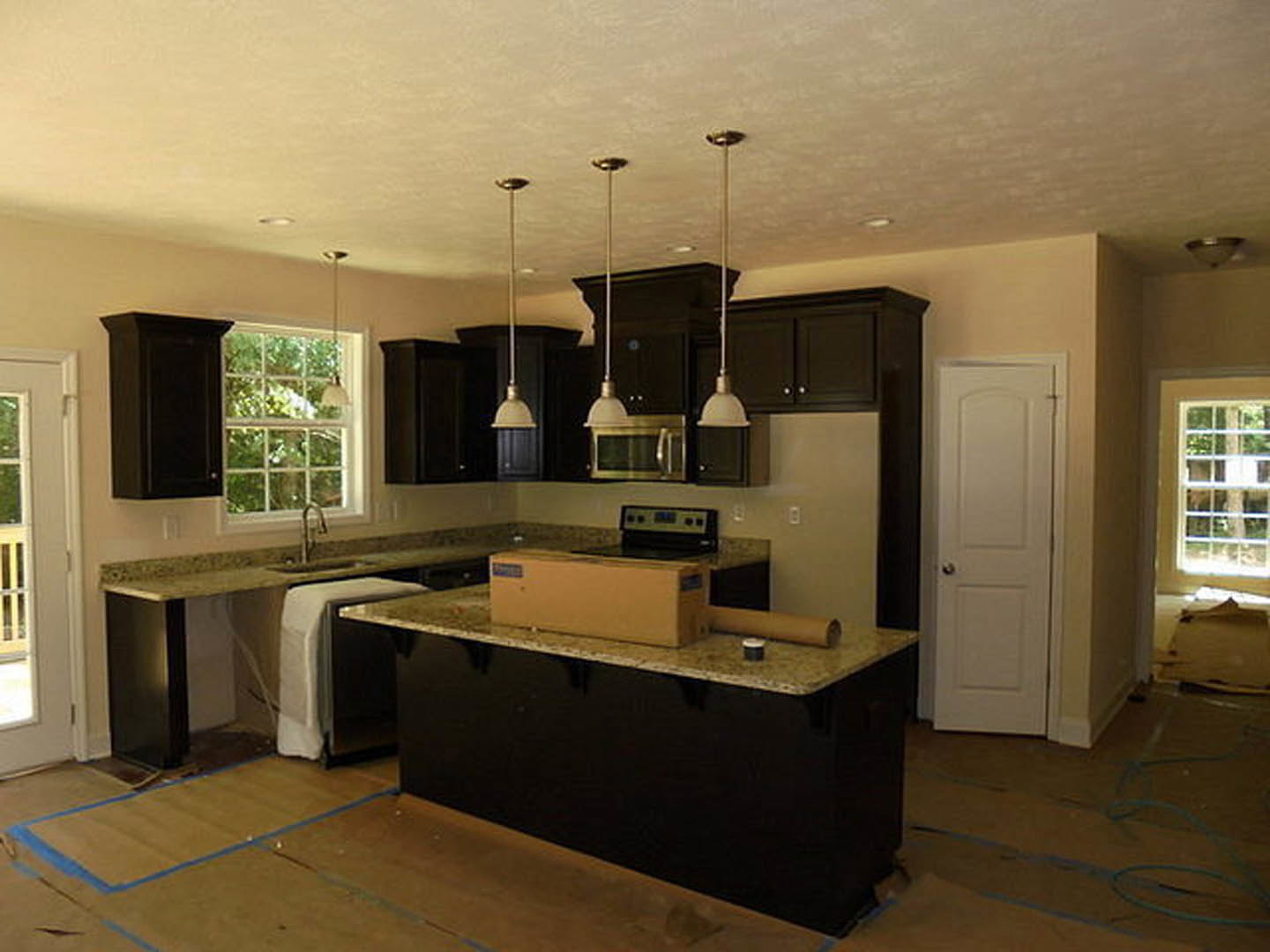 Black kitchen cabinets with sleek hardware, white countertops, tile backsplash, stainless steel sink, and a white door with a silver handle.