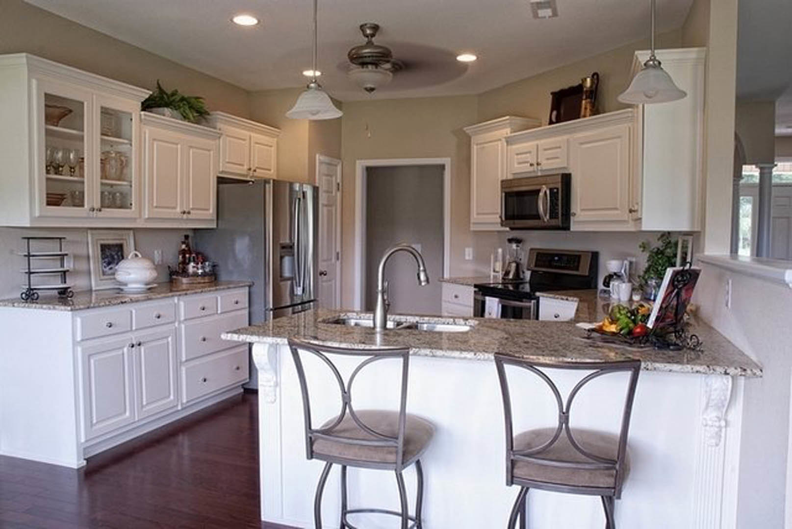 White kitchen cabinets with stainless steel microwave, cushioned dining chair, white bowl on table, and light countertops