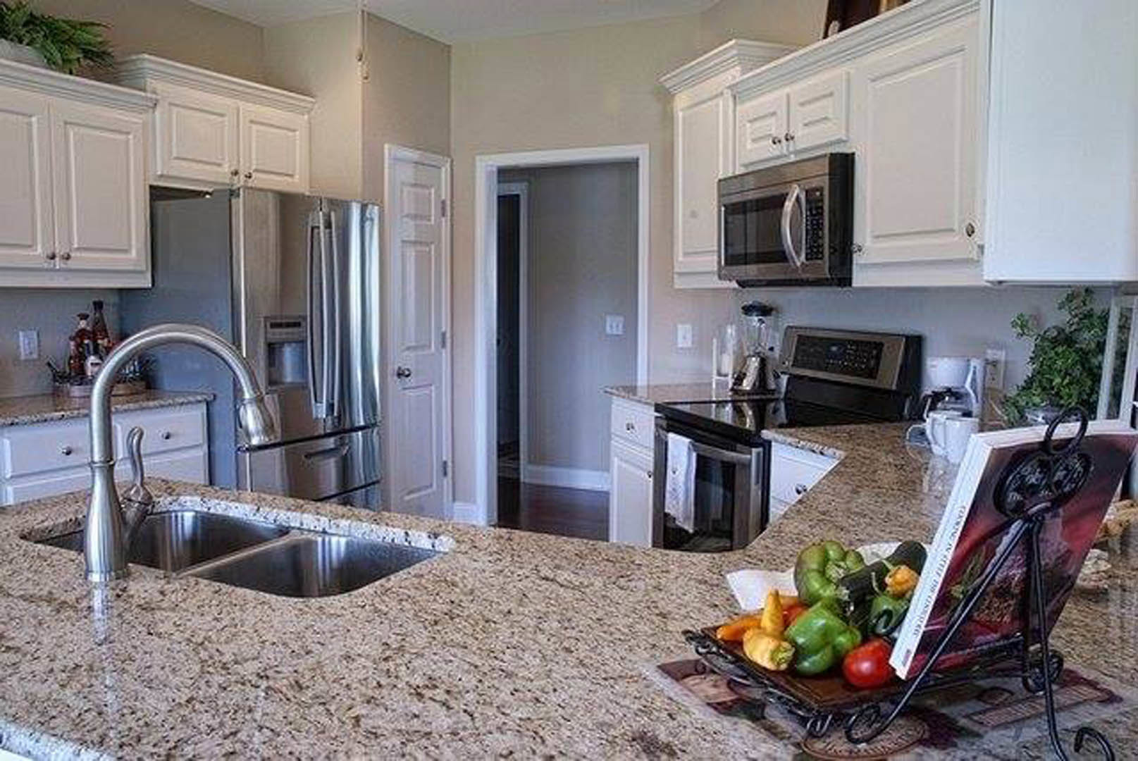 Granite kitchen countertops with a bowl of fruit, stainless steel refrigerator, microwave, oven, white cabinetry, and a green plant on the counter