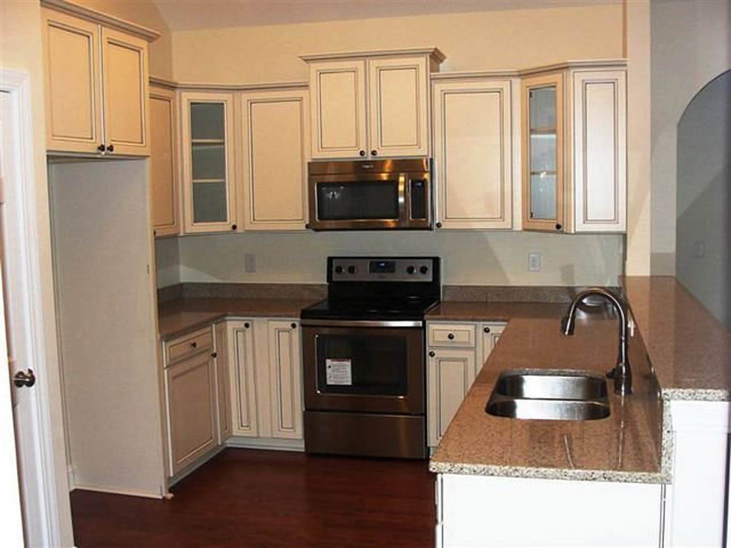 White shaker cabinets, stainless steel stove and microwave, light quartz countertops, tile backsplash, and neutral painted walls