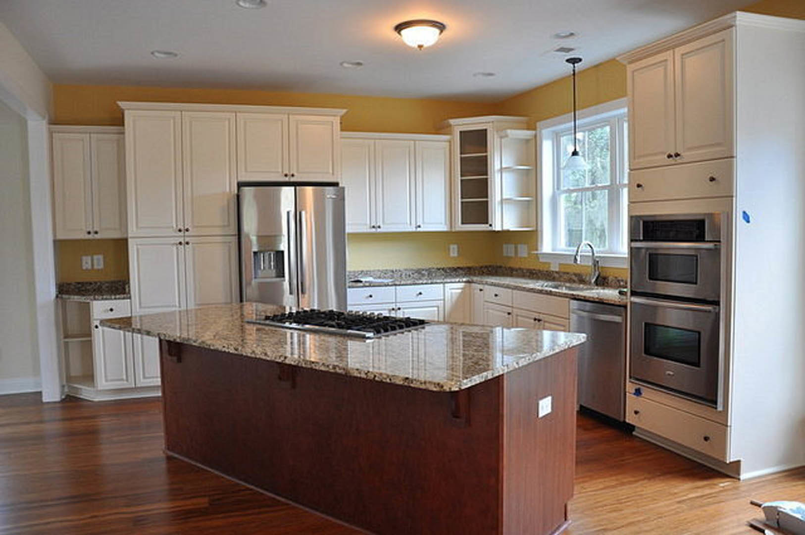 White kitchen cabinets, granite island countertop, stainless steel appliances including refrigerator, microwave, and oven, light wood flooring, undermount sink, and modern