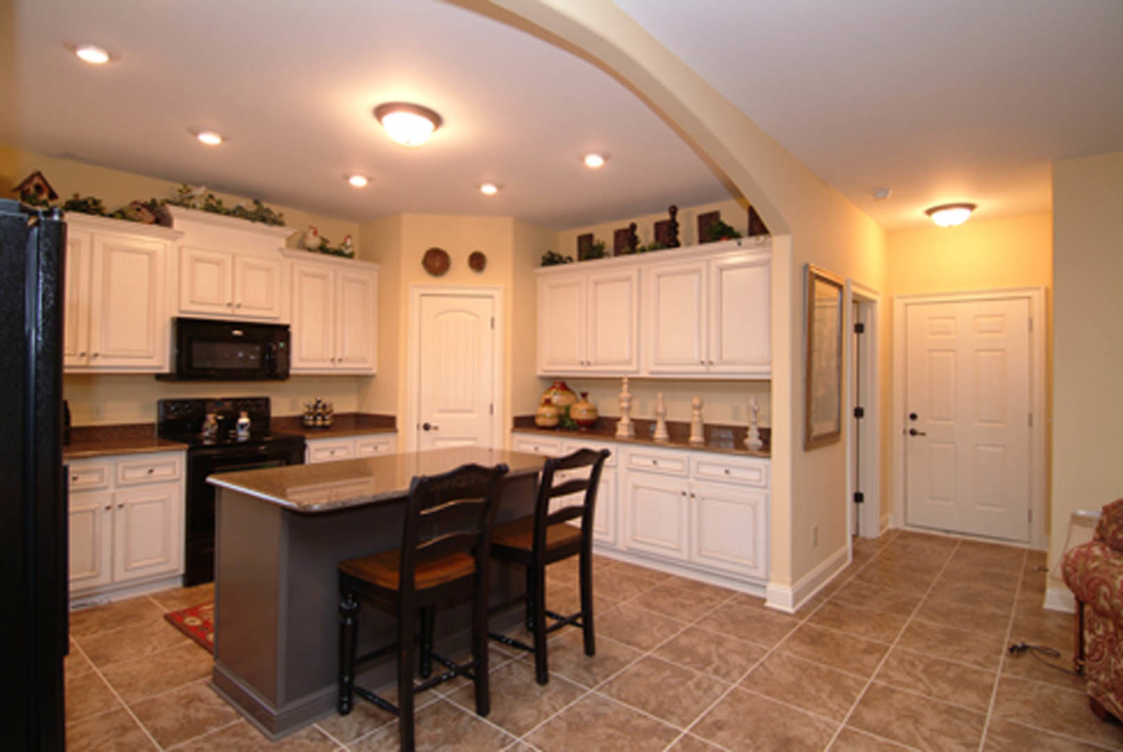 Open-concept kitchen featuring wood cabinetry, stone countertops, dining table with chairs, pendant lighting, and neutral tile flooring