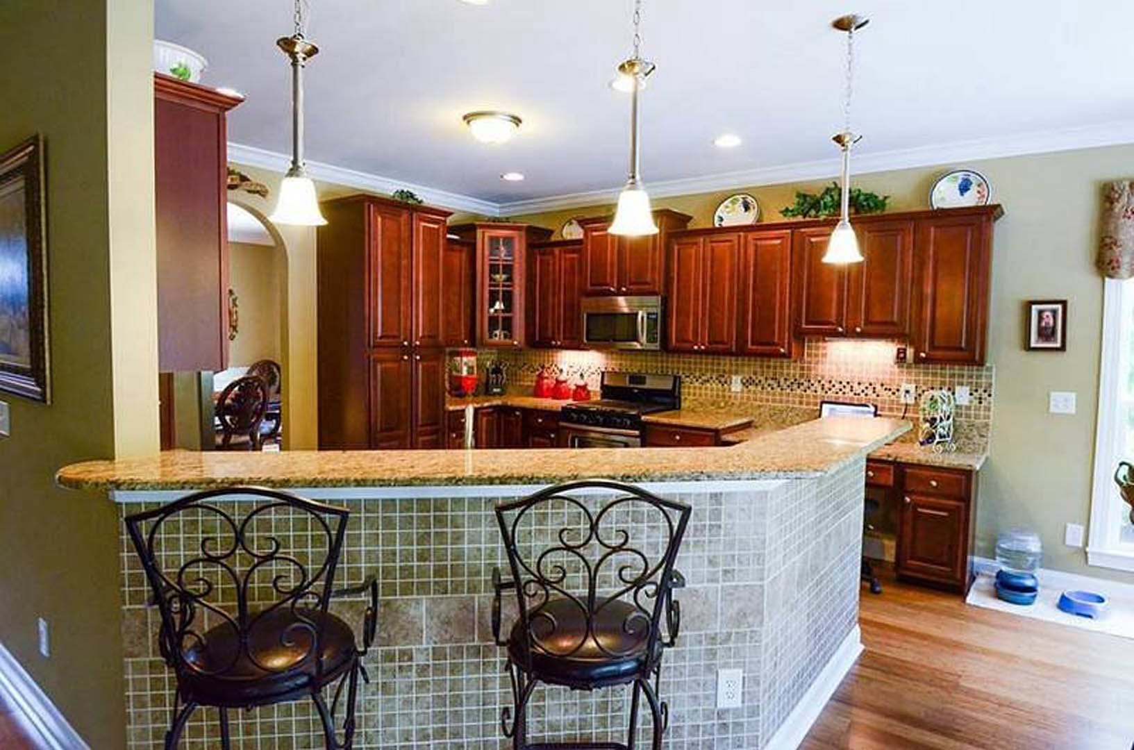 Open-concept kitchen featuring a bar-height counter with upholstered chairs, white cabinetry, stainless steel microwave and stove, light stone countertops, and a white electrical