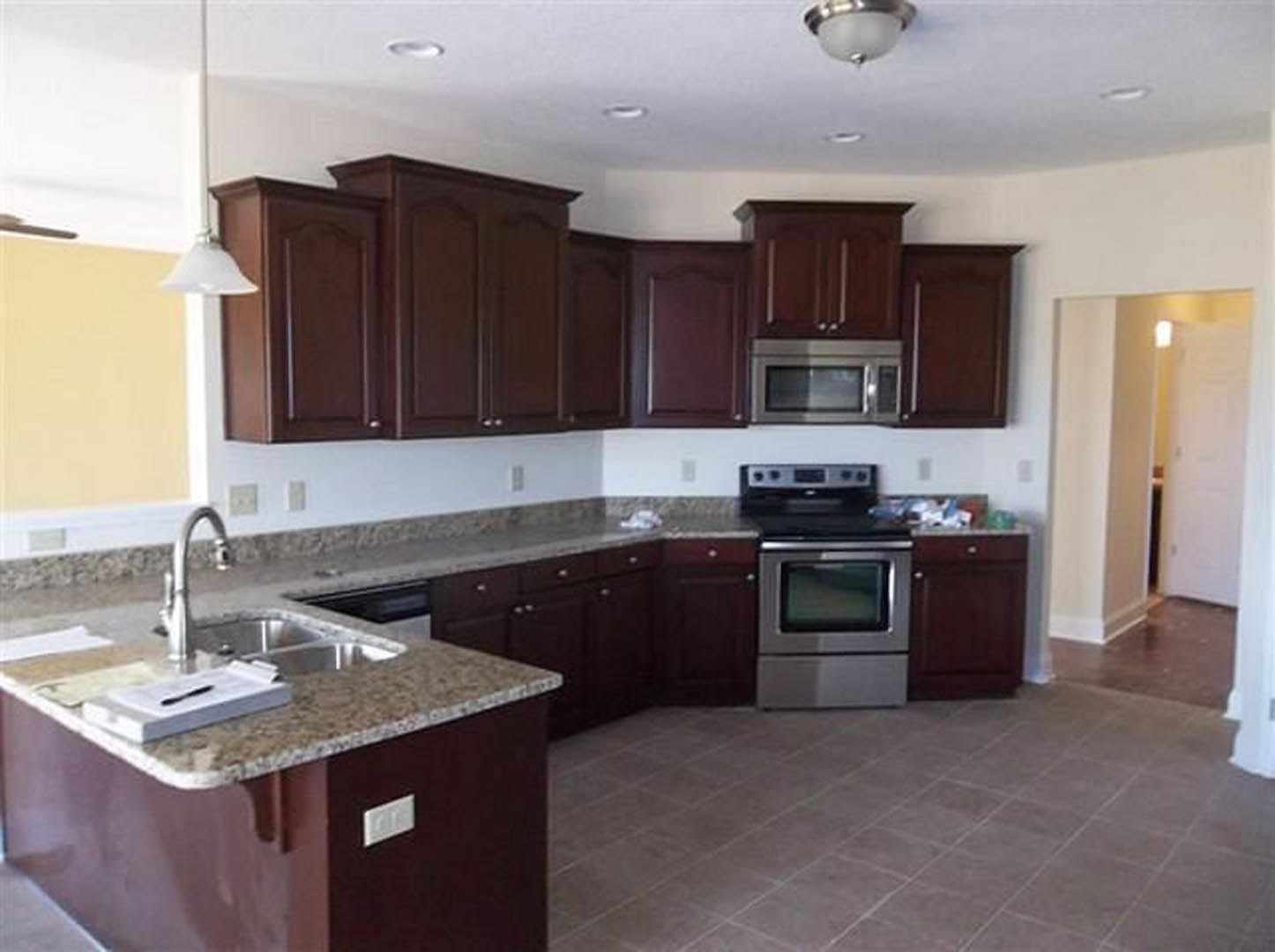 Kitchen featuring dark wood cabinetry, granite countertops, stainless steel sink, tile backsplash, and built-in microwave