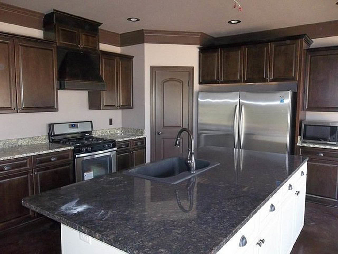 Granite countertop kitchen featuring stainless steel refrigerator, built-in microwave, stove, undermount sink, and white cabinetry