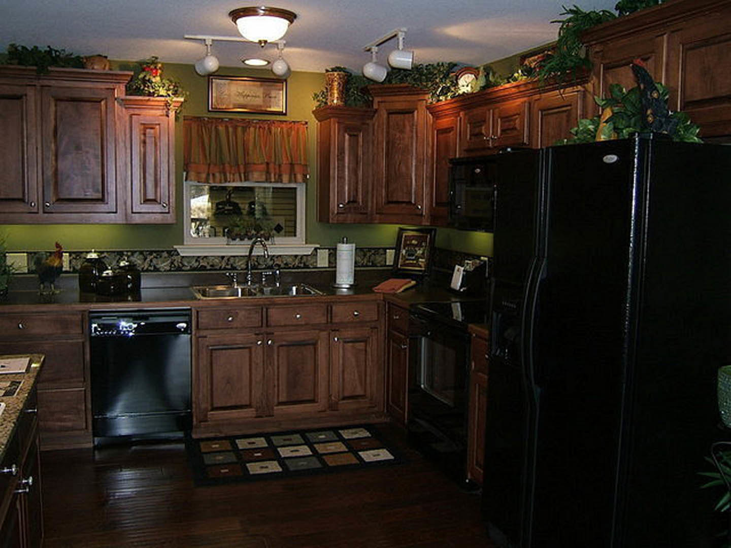 Modern kitchen with black refrigerator and stove, white cabinetry, stone countertops, and wood flooring