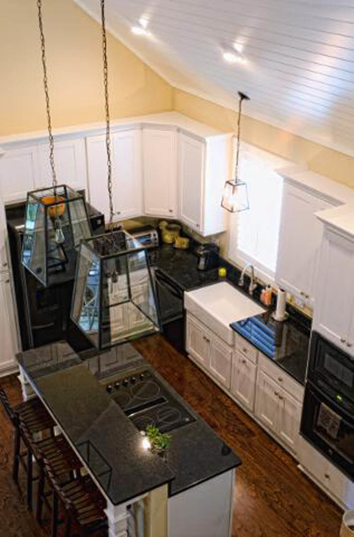 Black quartz countertops, white shaker cabinets, stainless steel sink, light wood flooring, modern appliances, neutral wall paint