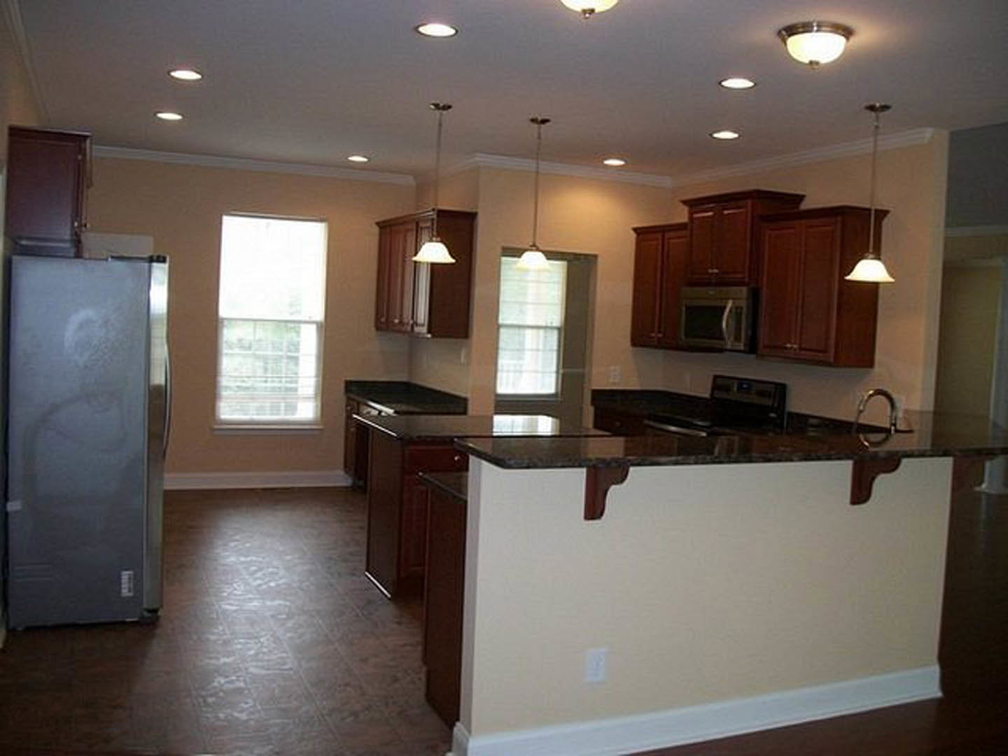 Modern kitchen featuring two stainless steel refrigerators, white cabinetry, stone countertops, built-in microwave with handle, light wood flooring, and large windows with white