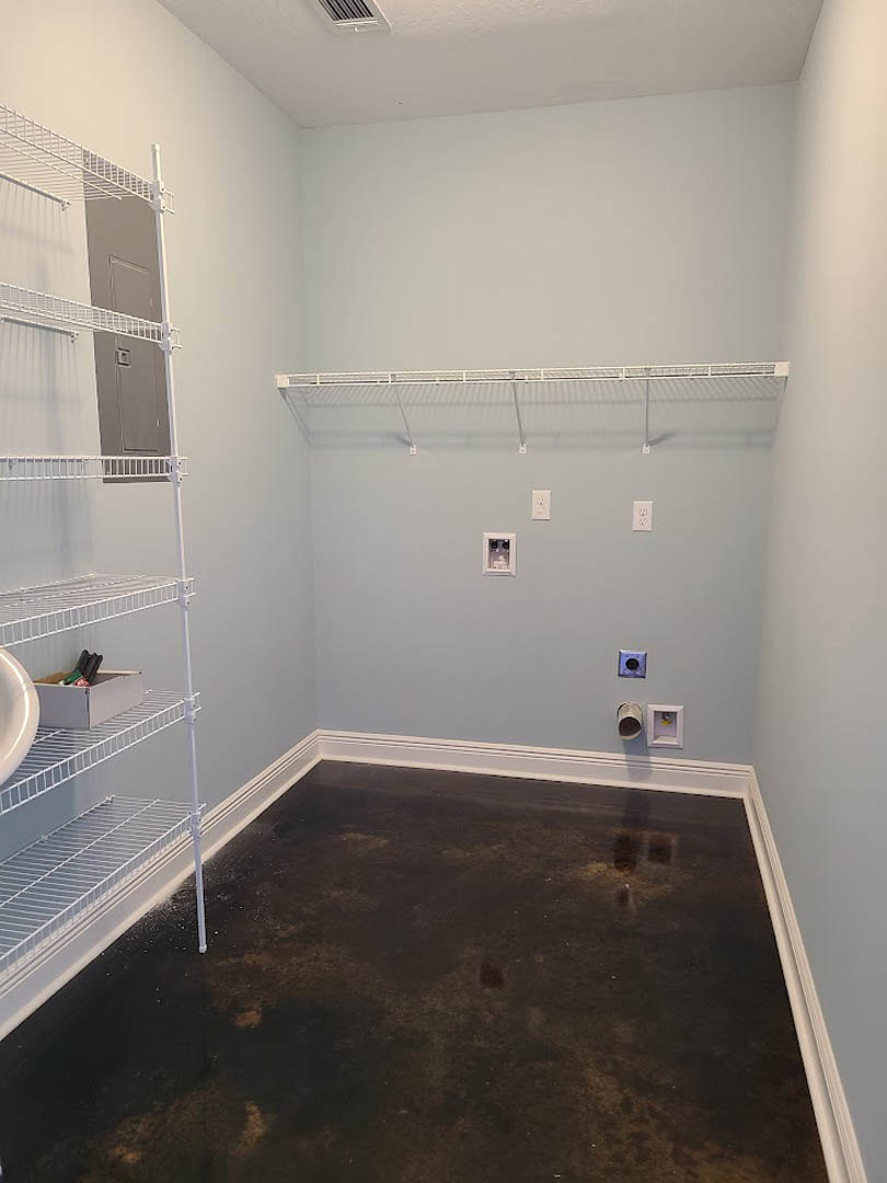 Black tile floor with white shelving units, white baseboards, metal shelf supports, white ladder leaning against a cabinet, and a white storage box containing assorted items.
