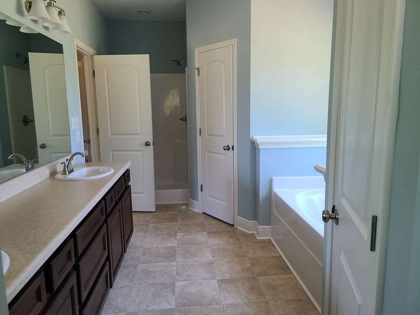 Bathroom with freestanding bathtub, white vanity and sink, large wall mirror, silver faucet, white paneled door with silver knob, light gray tile floor