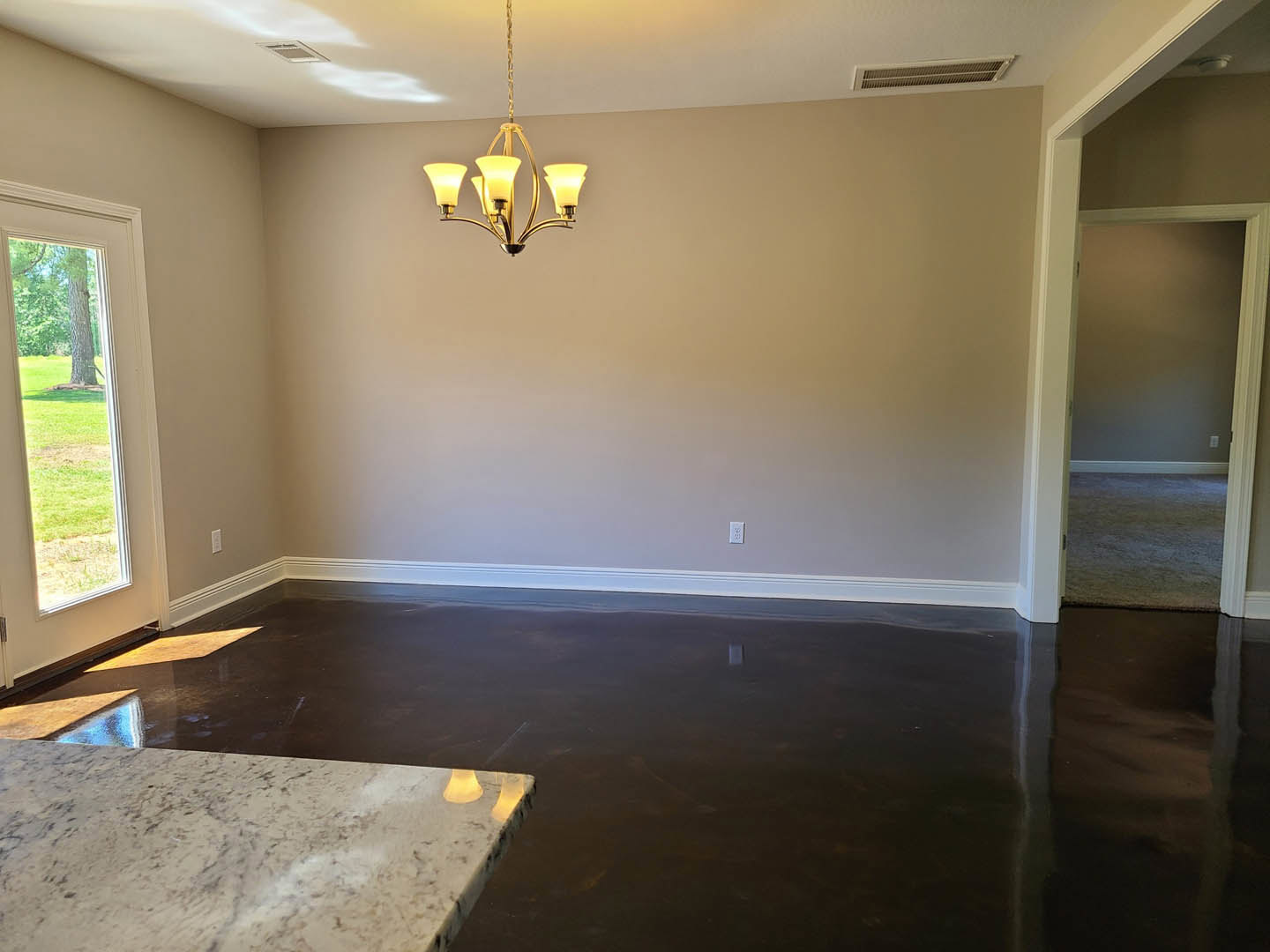 Marble dining table beneath crystal chandelier, white plaster walls, hardwood flooring, large window with view of leafy tree
