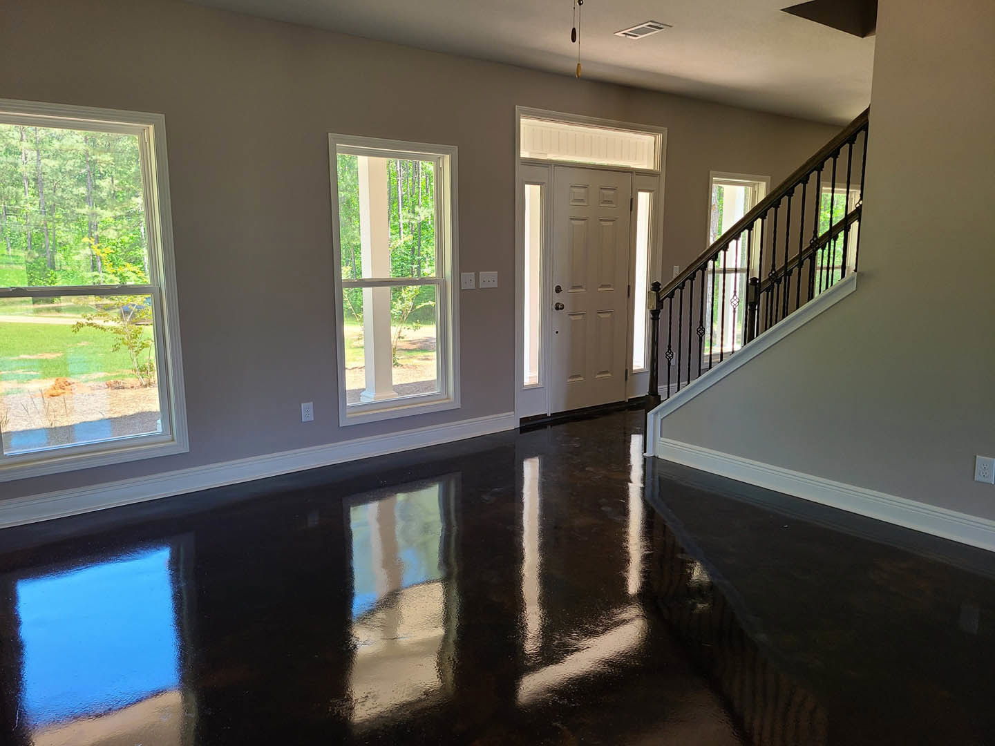 Hallway with polished wood floor, black metal staircase railing, large windows overlooking trees, white door with glass panels, blue accent square on black surface