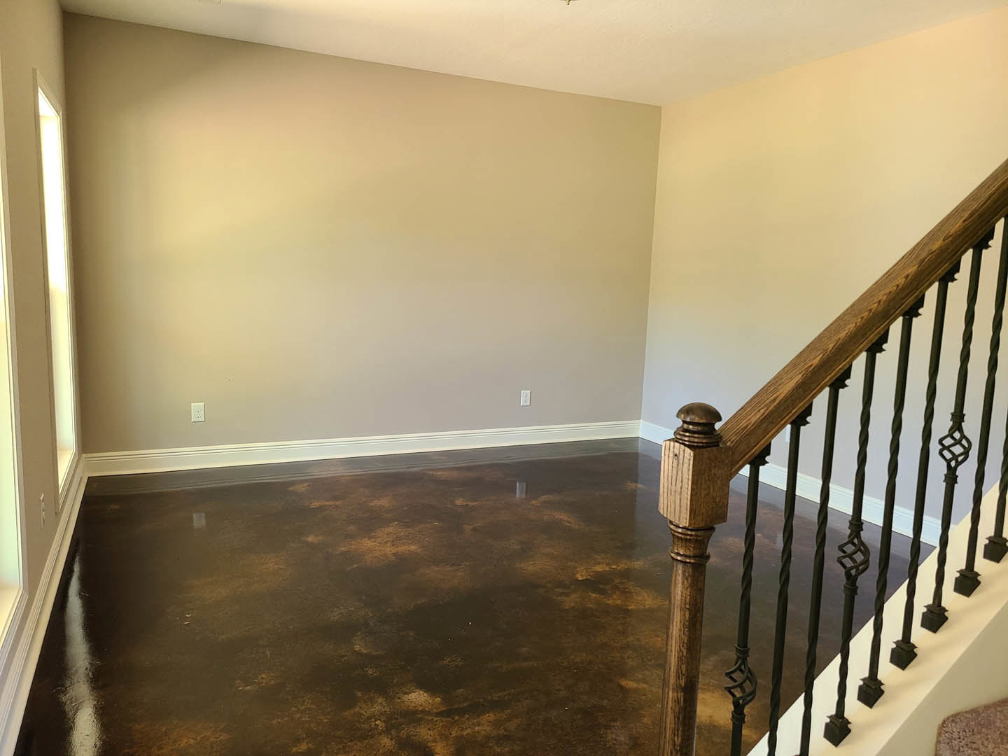 Curved wooden staircase with matching handrail, brown hardwood floor, white baseboards, plaster walls, and wall-mounted light fixture in a residential interior.
