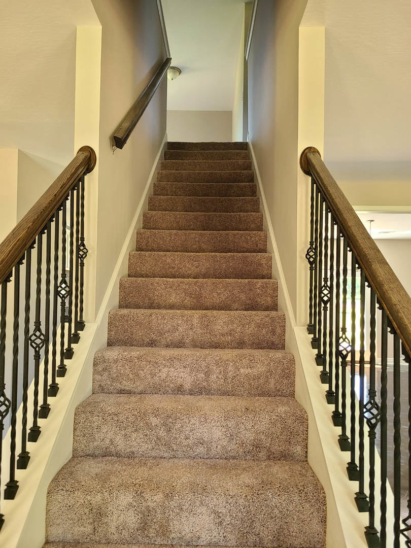 Carpeted staircase with metal railings, white walls, and wood handrail in a residential interior