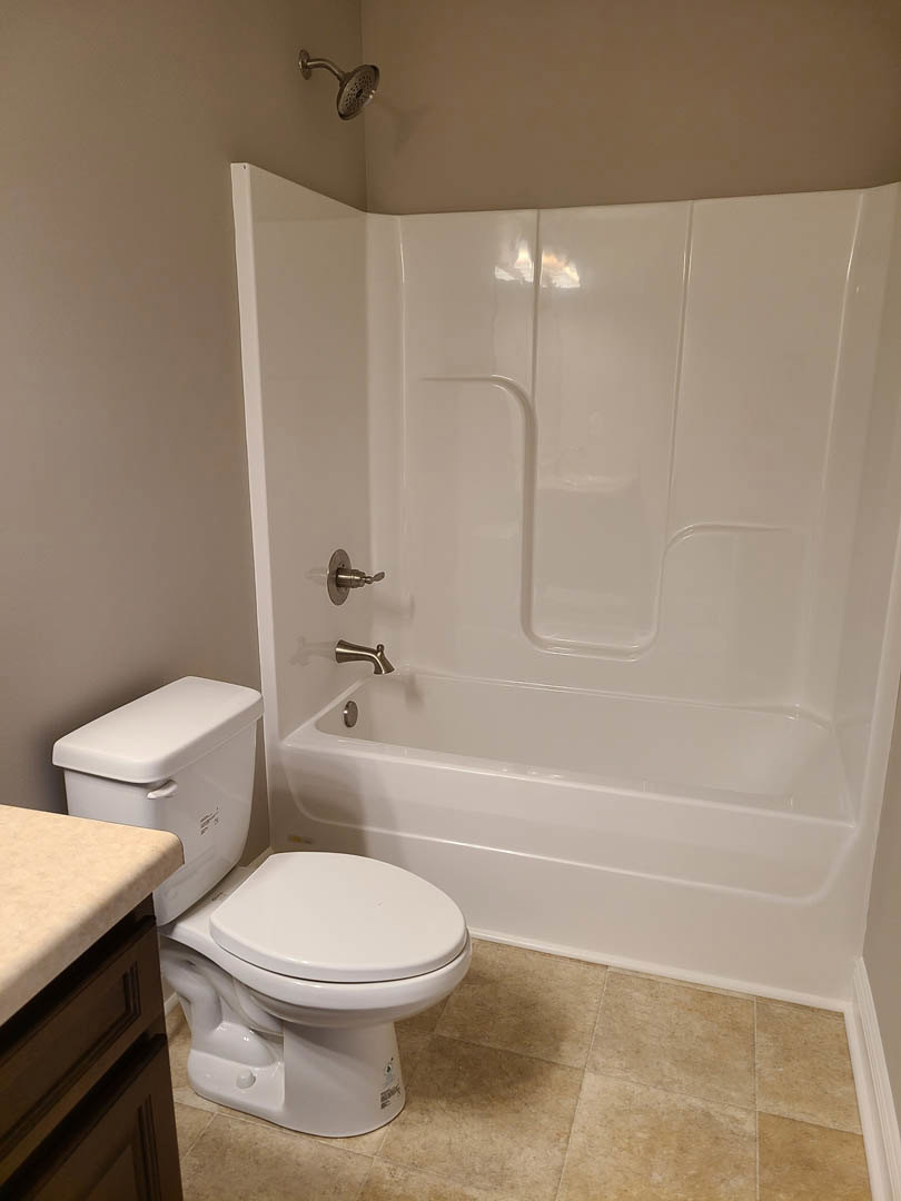 White bathtub and toilet beside a tiled wall, chrome shower head, and light-colored countertop in a modern bathroom.