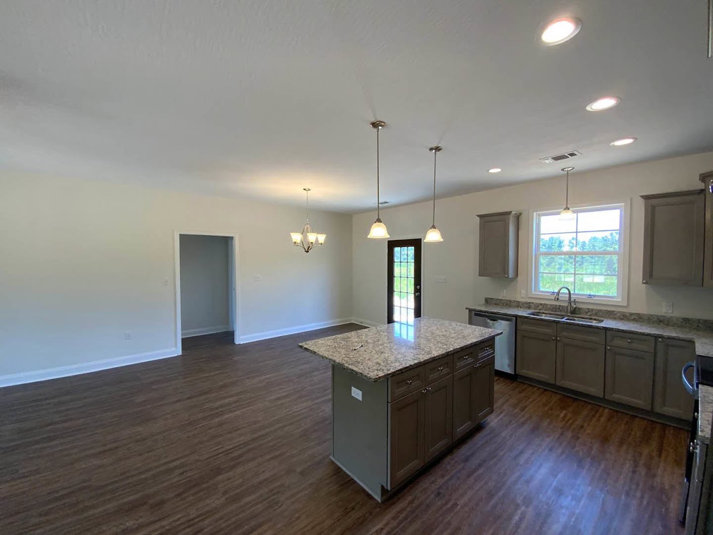 Kitchen with wood flooring, central island featuring granite countertops, white cabinetry, stainless steel sink beneath a window overlooking greenery, white walls and trim, and a