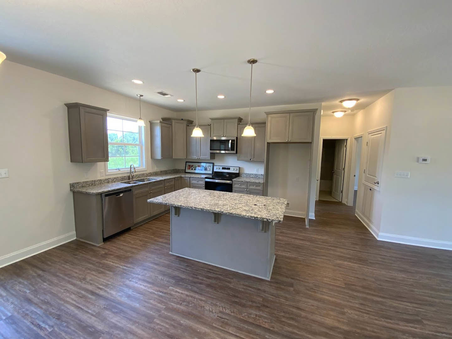 Spacious kitchen featuring a large granite island, stainless steel appliances including microwave and stove, white cabinetry, tile backsplash, laminate flooring, and a window