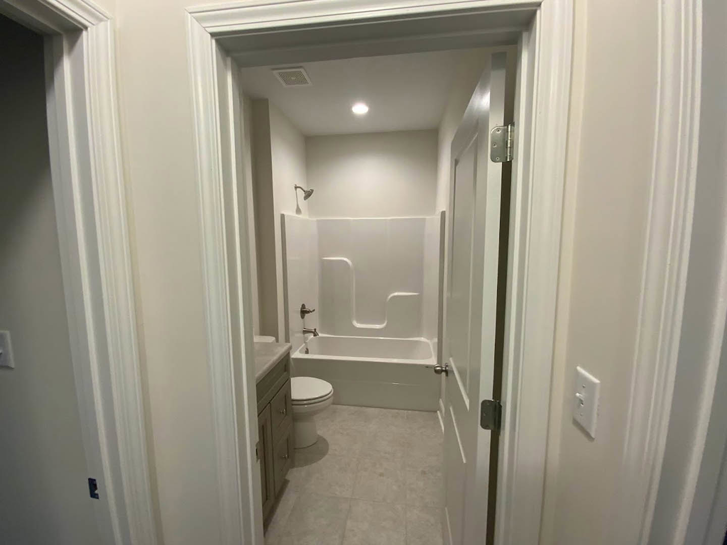 White tile bathroom with a white bathtub, toilet, and light-colored plaster walls; close-up of door handle and light switch visible.