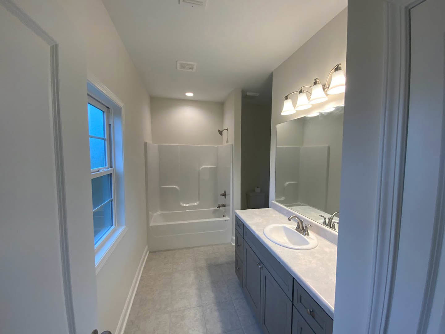 Modern bathroom featuring a white bathtub, tiled walls, glass-enclosed shower, vanity with undermount sink, large framed mirror, overhead light fixture, and ceiling vent.