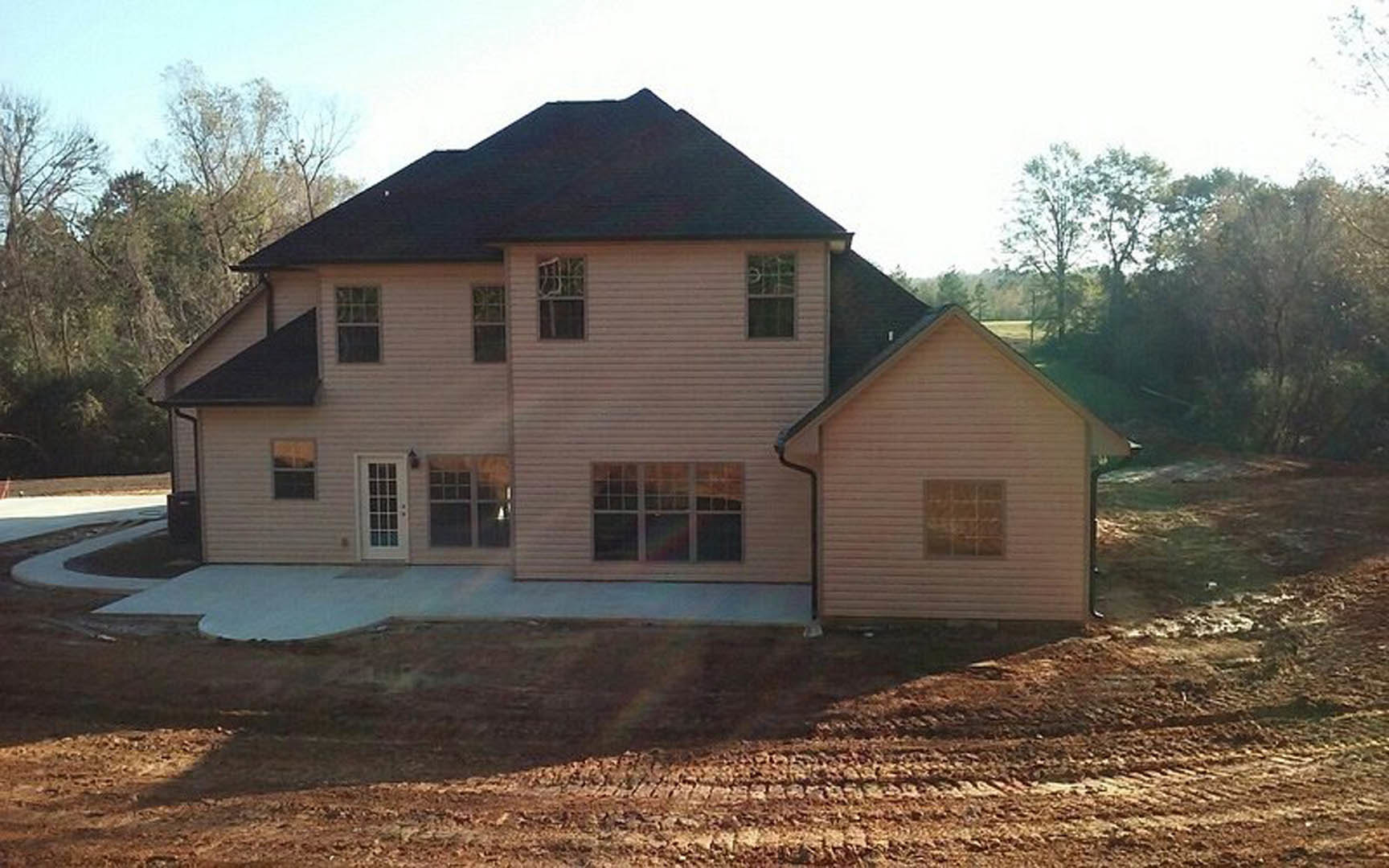 Partially built house with black roof, multi-pane window, and unfinished door, surrounded by dirt field and sparse vegetation