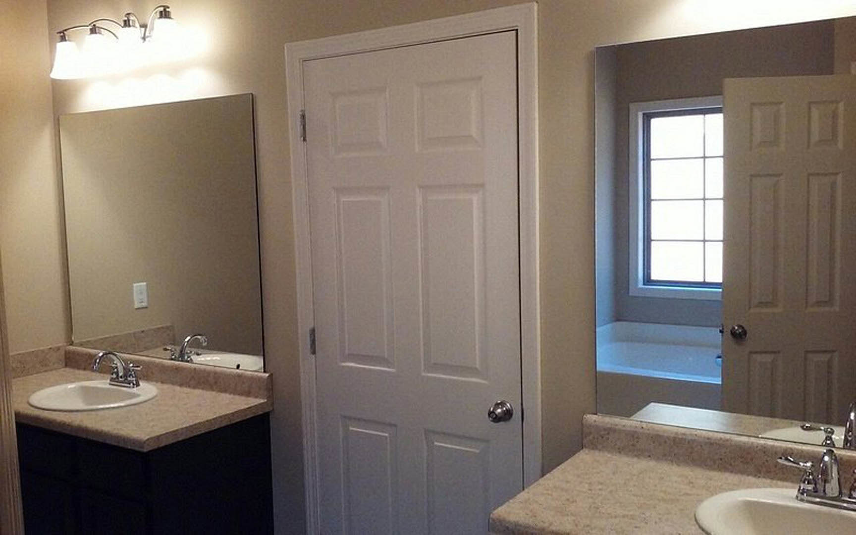 Bathroom with two undermount sinks set in a stone countertop, white paneled door partially open, tile flooring, chrome faucets, and neutral wall finishes