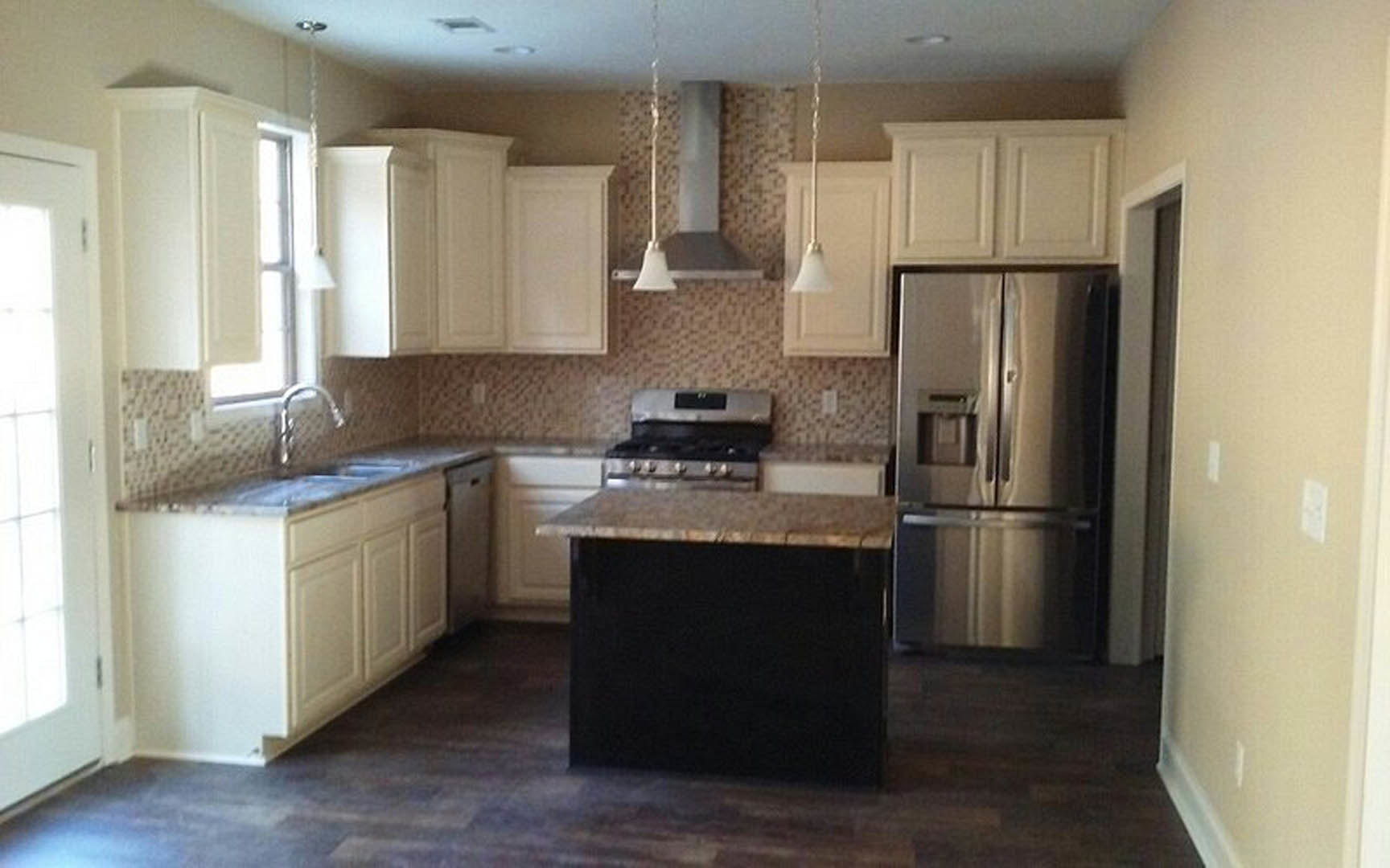 White kitchen with shaker cabinets, black island with waterfall countertop, stainless steel appliances, tile backsplash, and wood flooring