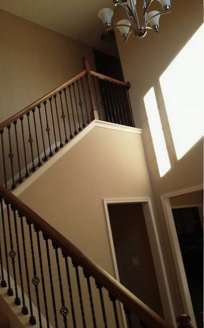 Hardwood staircase with white balusters, adjacent to a paneled door and open doorway, surrounded by plaster walls and crown molding