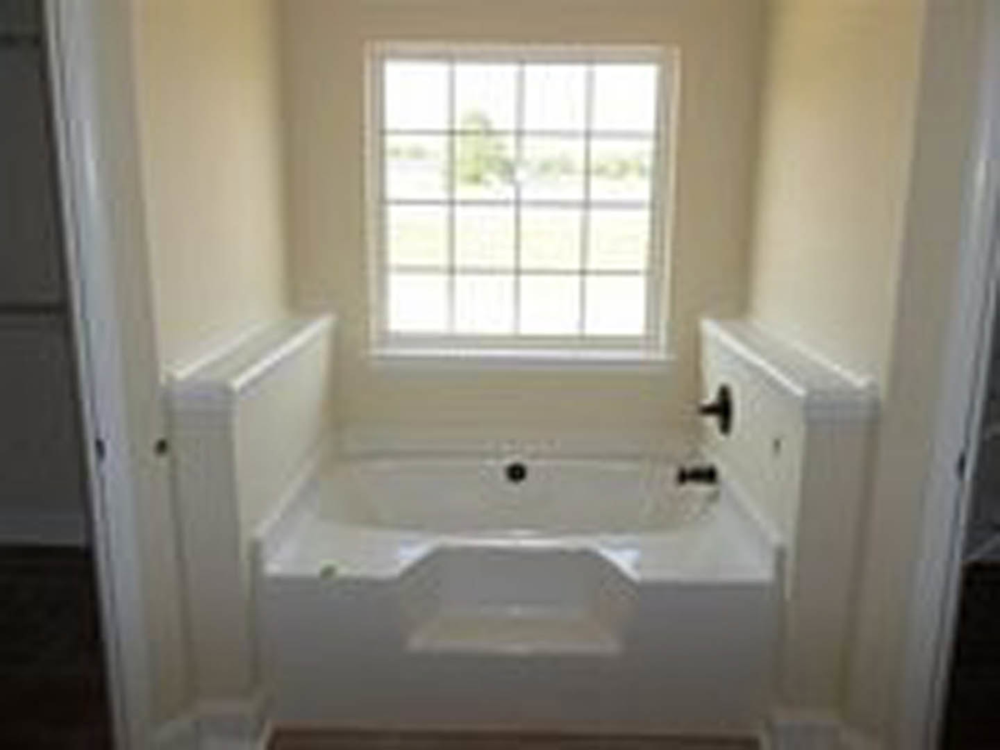 Freestanding white bathtub with matte black faucet, gray tile floor, large window, and light-colored walls