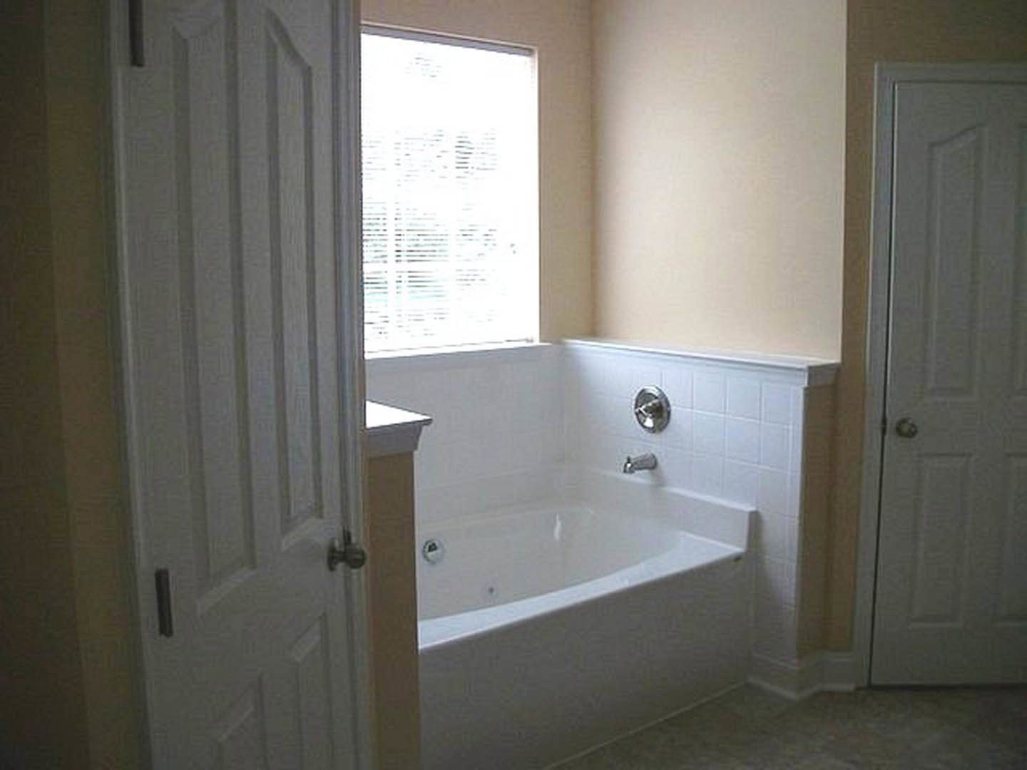 White freestanding bathtub beneath a large window, gray tile walls, chrome faucet, glass shower enclosure, white sink with modern fixtures