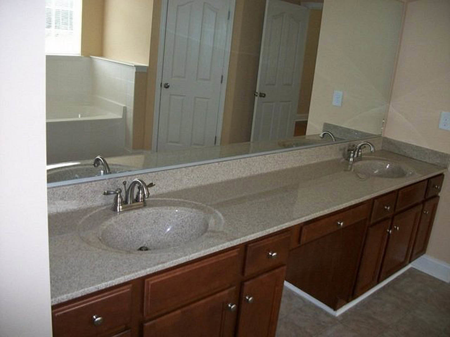 Bathroom with two undermount sinks set in a stone countertop, freestanding bathtub, tiled walls, wood cabinetry, chrome faucets, and large mirror.