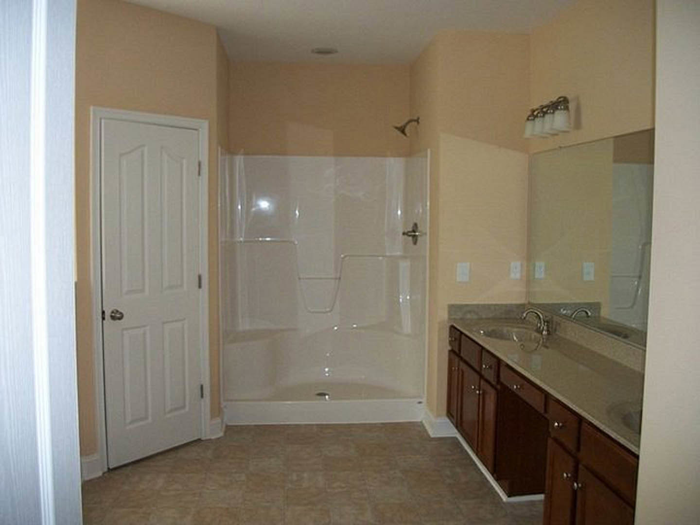 Modern bathroom featuring a glass-enclosed shower, white sink with chrome faucet, light tile flooring, and white cabinetry
