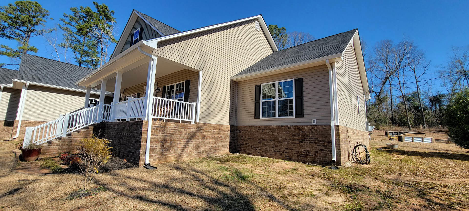 Two-story house with white framed windows, white porch railing, covered front porch, green lawn, and mature tree in yard