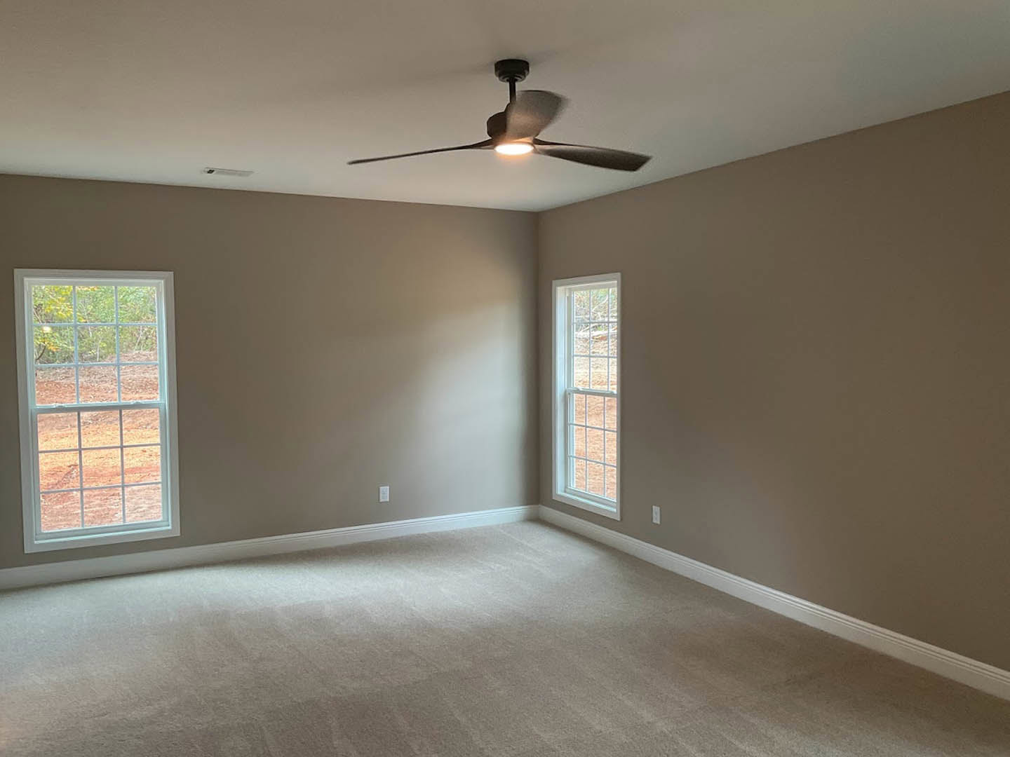 Carpeted room with white walls, multi-pane windows, ceiling fan with light fixture, and natural daylight illuminating the space