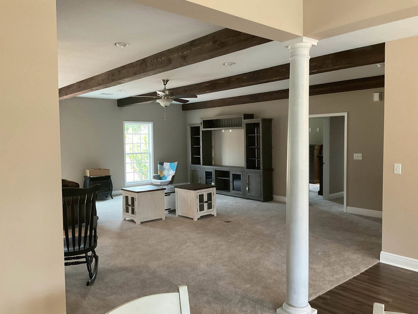 Living room with white ceiling, white coffee table, white pillar, chair, window with multiple square panes, white cabinet with glass doors, and white and black cabinet