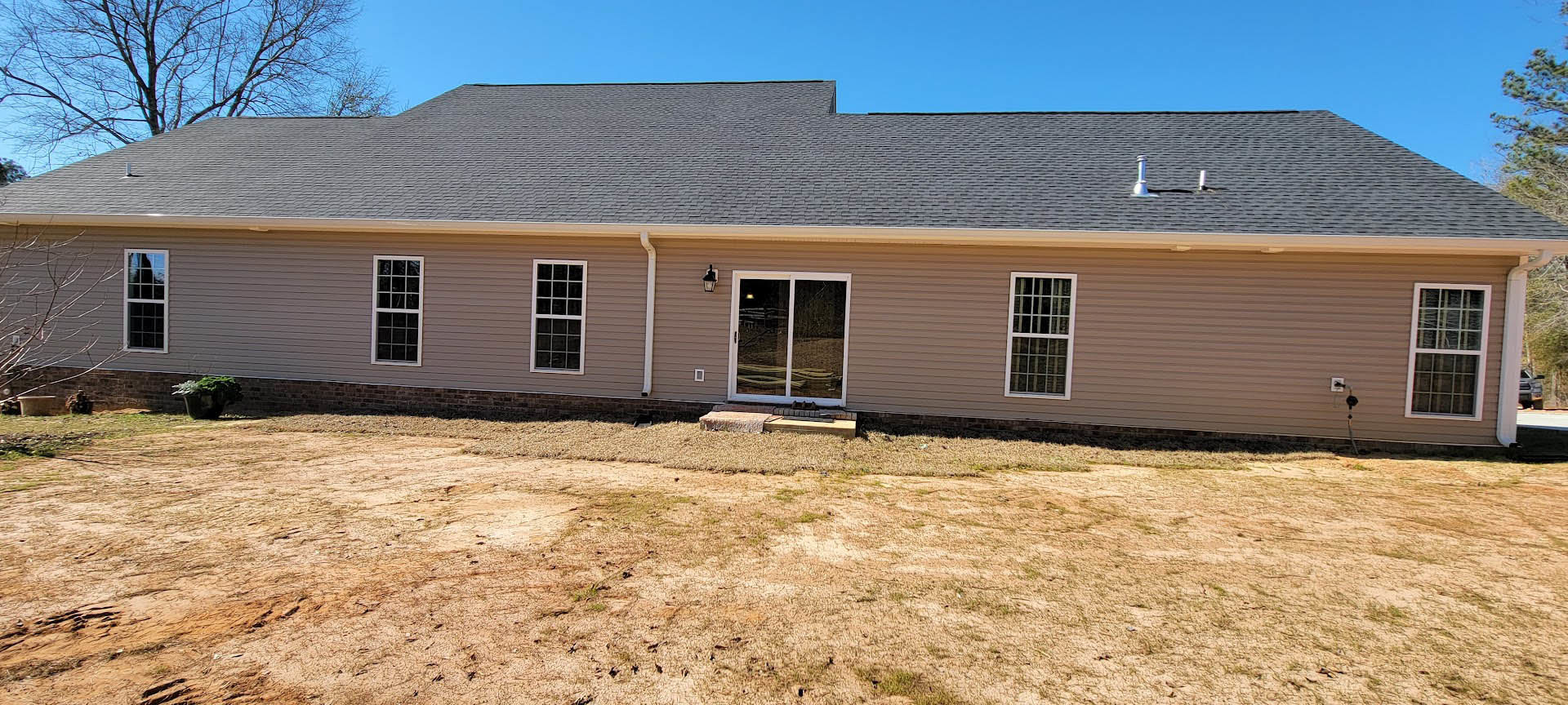 Modern house with white siding, sliding glass door with white frame, multi-pane window, brick retaining wall, dirt yard, and planter with green leafy plants